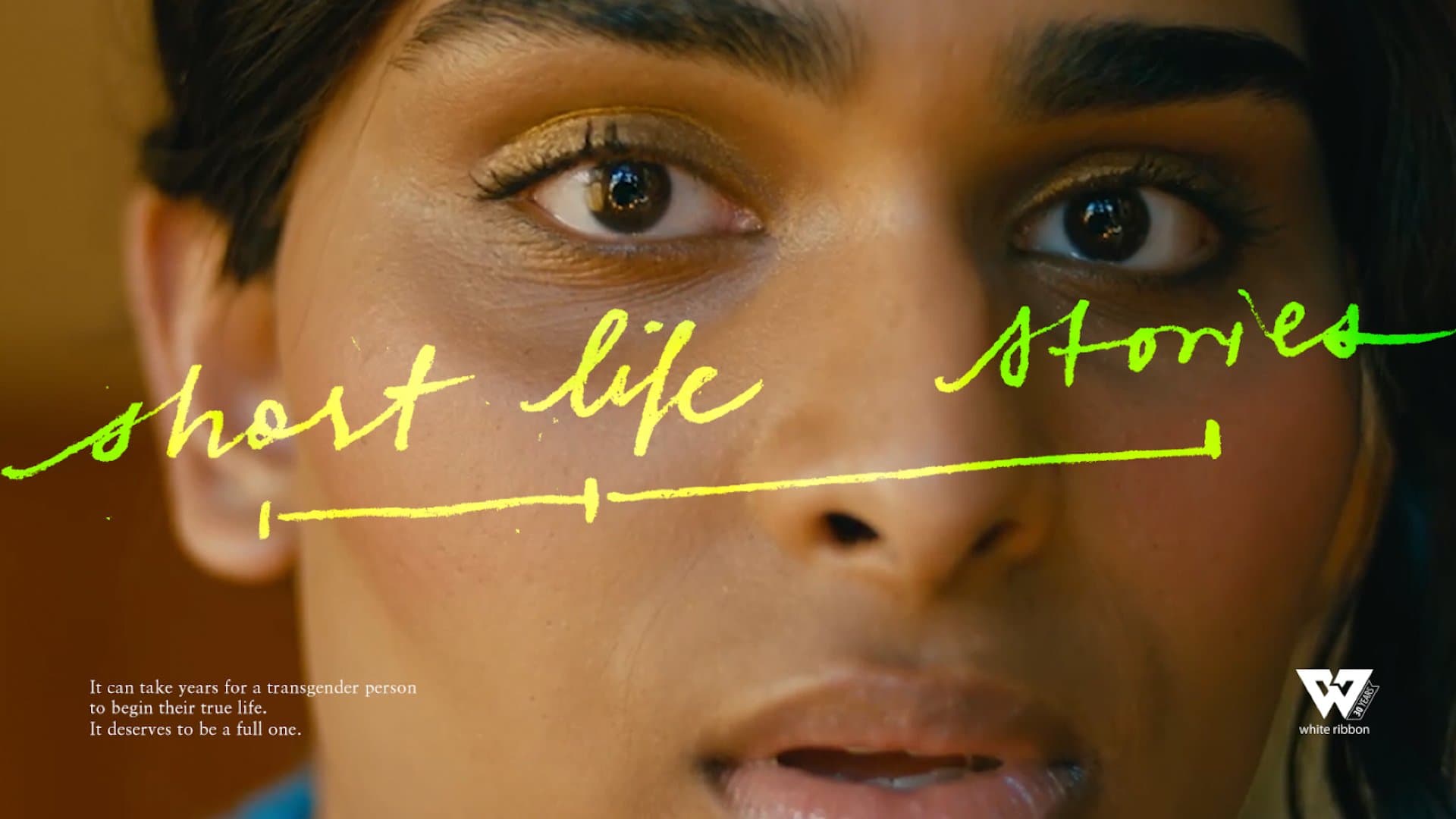 A still from the spot featuring the protagonist's face, with the title "Short Life Stories" written across their face, a White Ribbon logo, and some descriptive copy reading "It can take years for a transgender person to begin their true life. It deserves to be a full one."